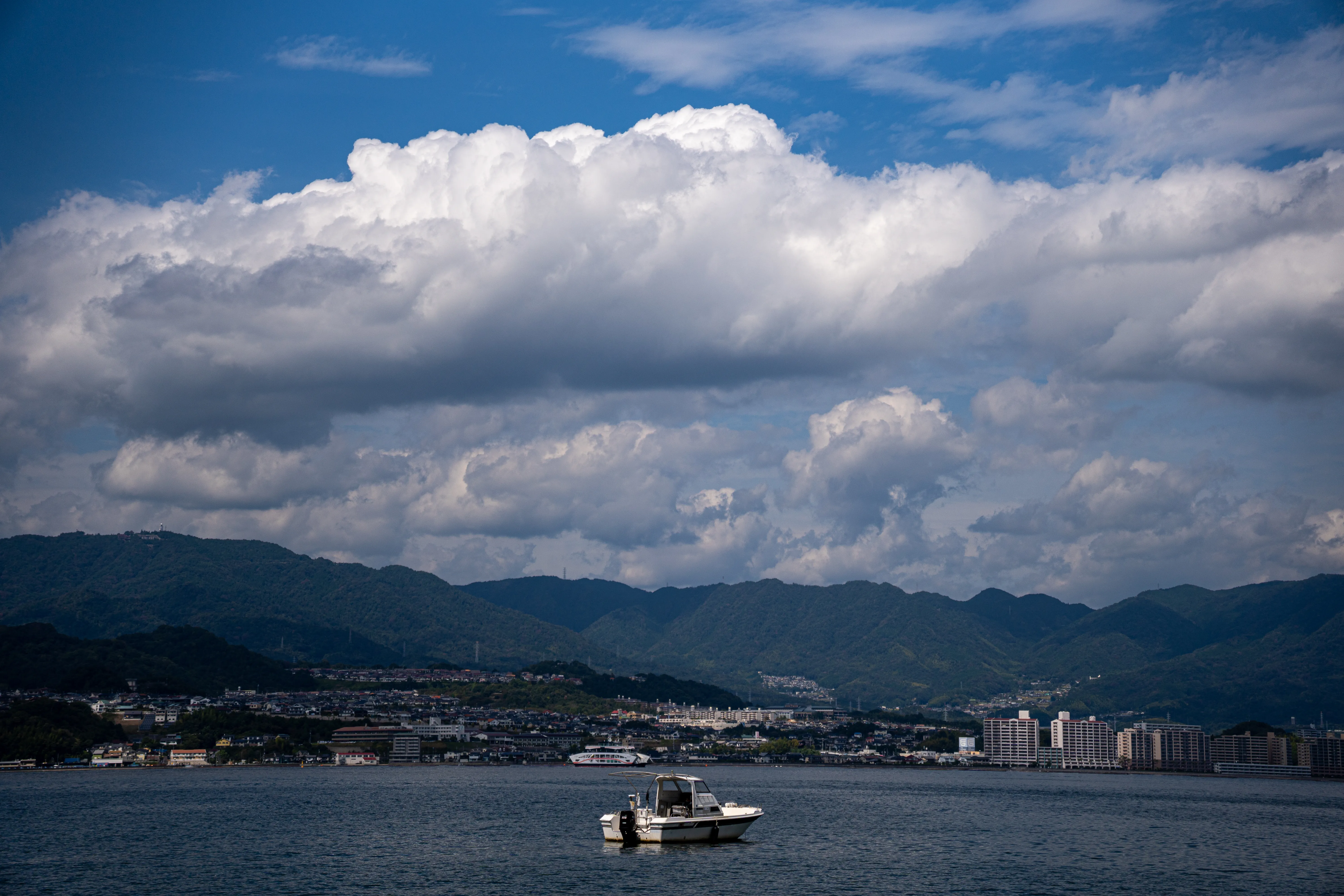 A boat on the water beneath towering clouds and mountains